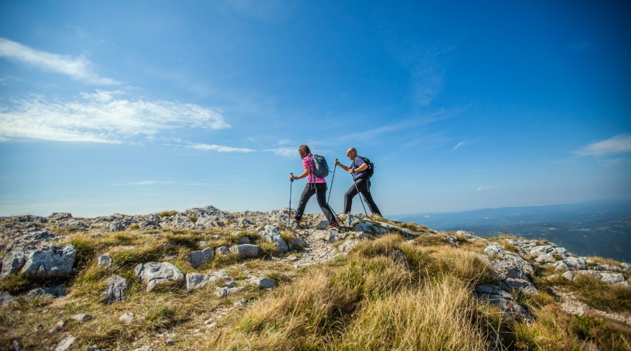Couple hiking on Nanos Plateau in Slovenia against a blue sky